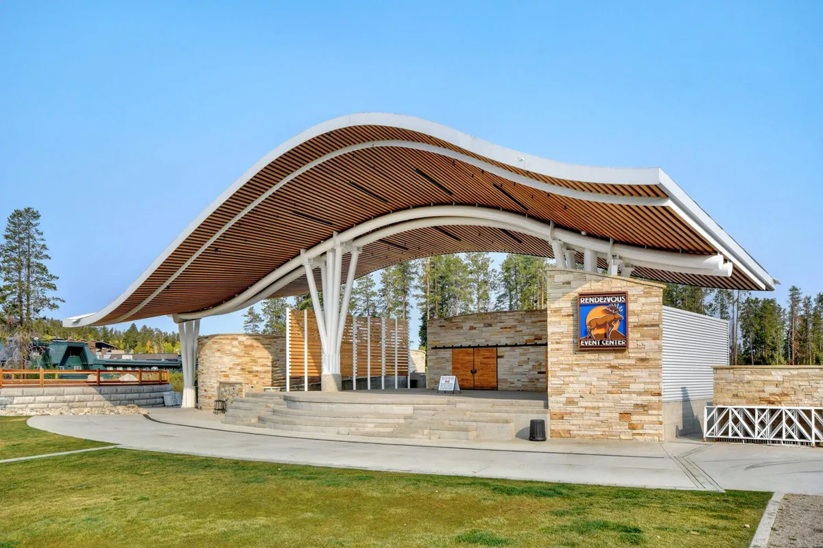 An exterior image of a modern event center with a distinctive curved roof and stone facade. The event center sign is visible, and the scene hints at outdoor spaces suited for concerts, festivals, and community events.
