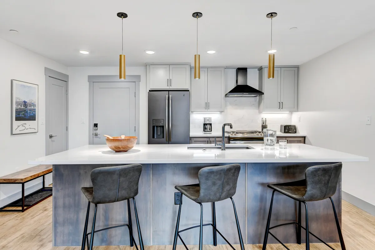 This image centers on the kitchen island, pendant lights, and stainless steel appliances. The granite countertops are visible, and a bowl sits atop the island. There is a sense of ample workspace, stylish finishes, and an inviting environment for cooking and socializing.