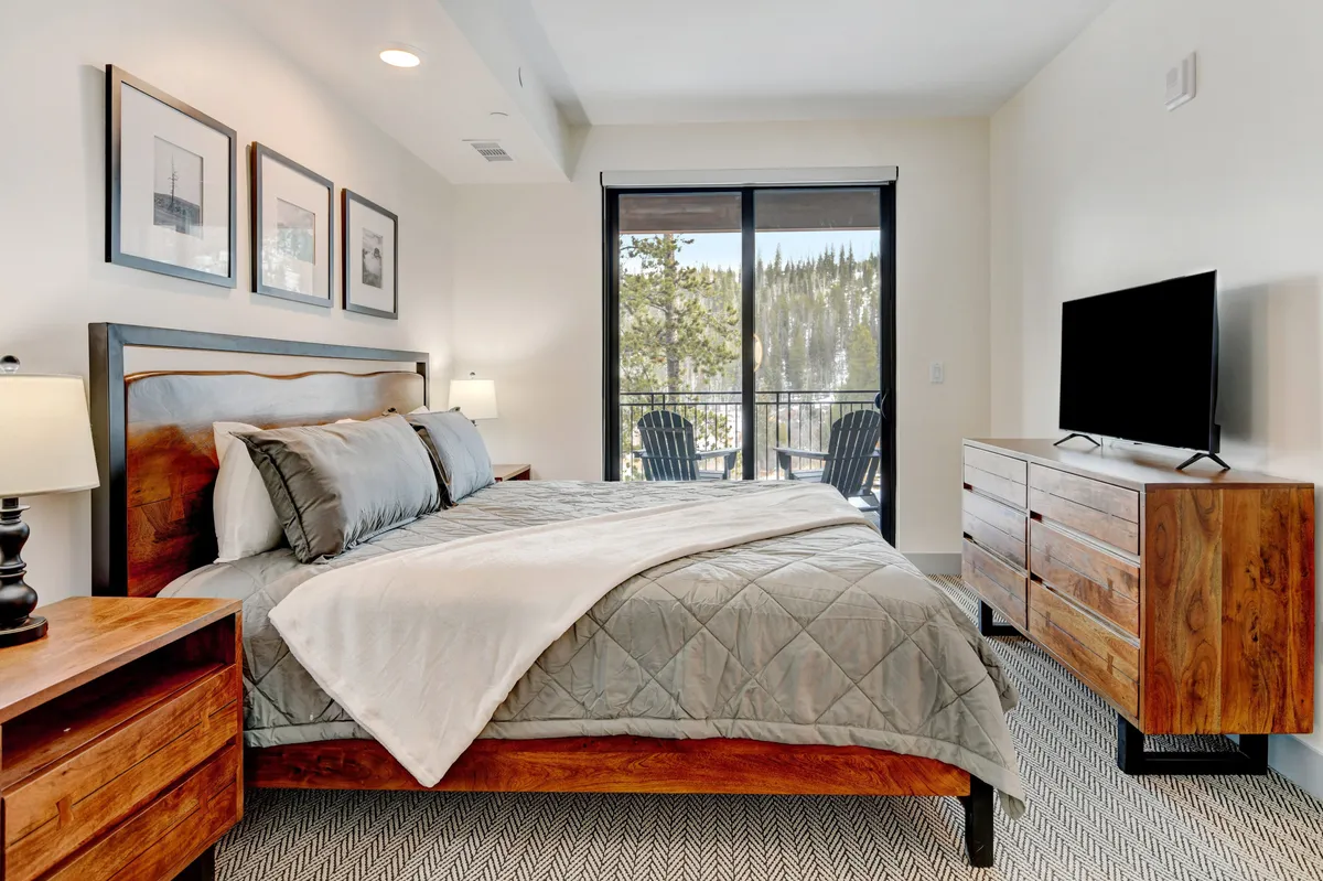 A serene master bedroom featuring a plush king bed, large window letting in abundant natural light, a dresser and nightstands, and a wall-mounted television perfect for movie nights. The room is styled for comfort and relaxation, with soothing decor and premium linens visible.