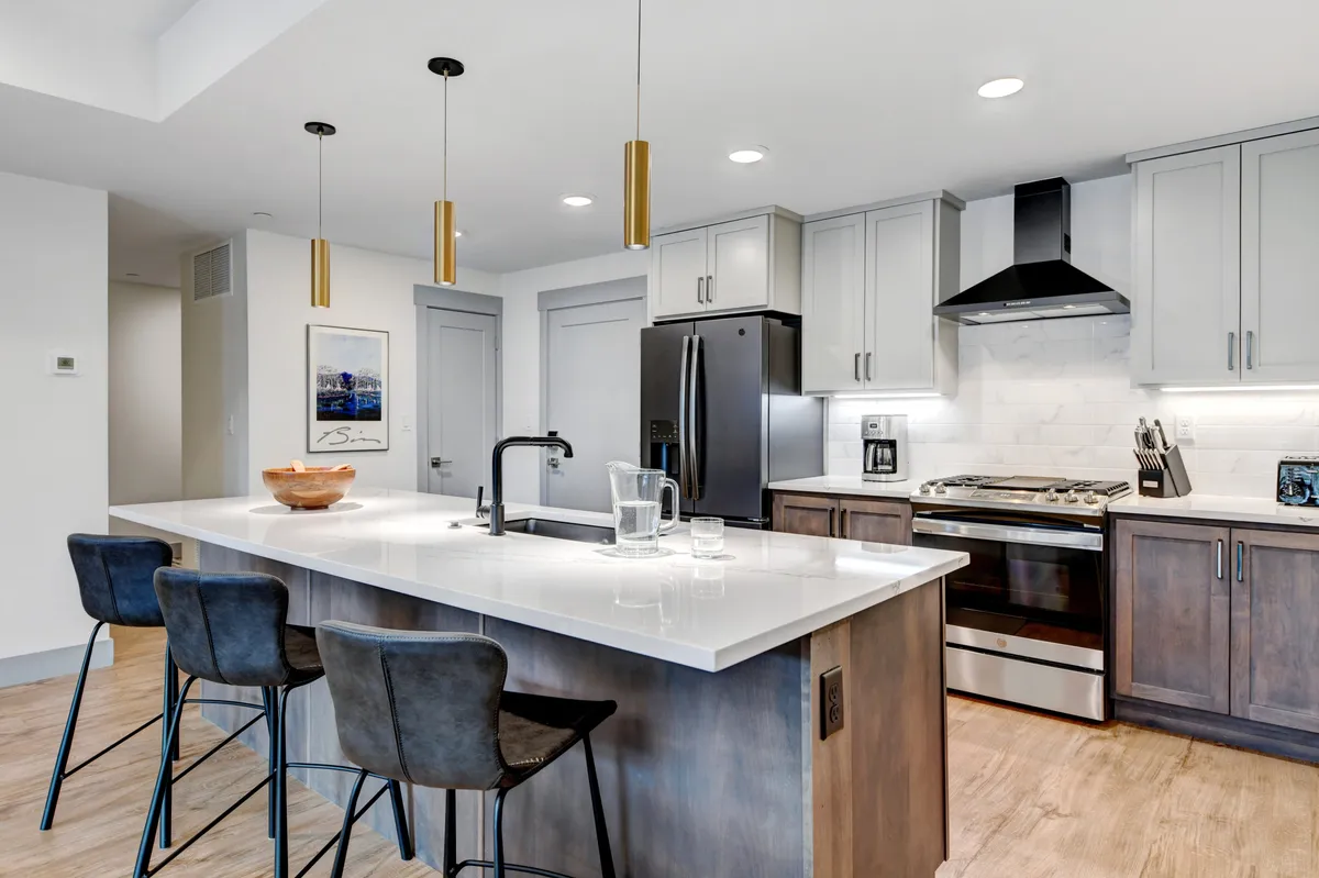 This image shows the kitchen from a slightly different angle, highlighting the island with stools, visible appliances, and an inviting layout that encourages both cooking and conversation. The contemporary design and cozy atmosphere enhance the sense of a welcoming space for preparing meals and gathering.
