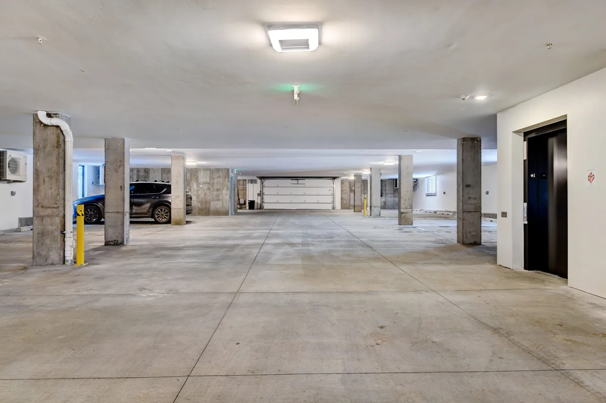 A clean, well-lit heated garage with multiple parking spaces, an elevator, and sturdy exposed columns. The environment is practical, with easy access for loading gear or vehicles, and conveys a sense of modern convenience and security.