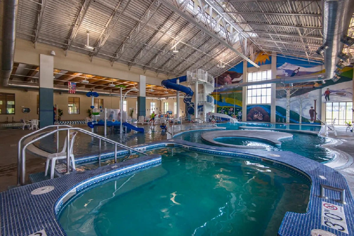 A vibrant, indoor recreational center featuring a swimming pool with colorful water slides and children playing joyfully in the water. The space is lively, packed with features for family fun, including murals and water features.
